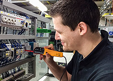 Um eletrotécnico para técnica operacional (em formação) controla componentes elétricos no laboratório de formação da STAHL CraneSystems.